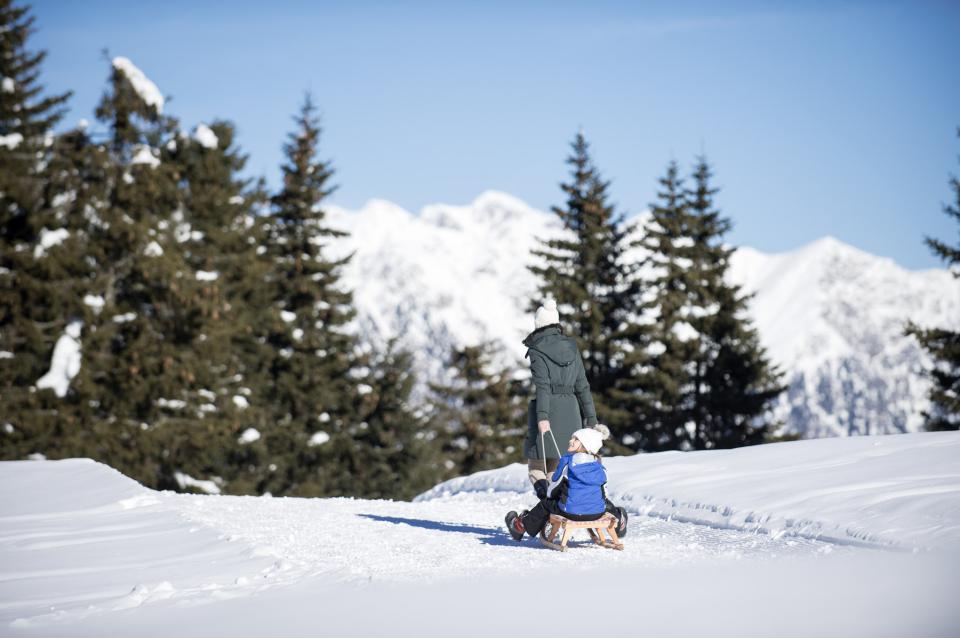 Frau zieht Kind auf dem Schlitten im Schnee